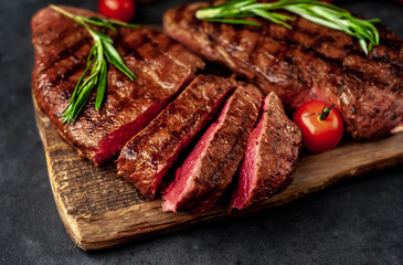 Tasty two grilled beef steaks with spices and herbs on a cutting board on a stone background