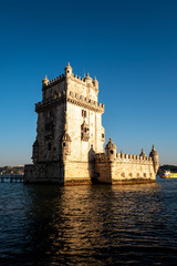 Obraz premium The tower of Belem in Lisbon illuminated by the setting sun with a boat passing in the background.