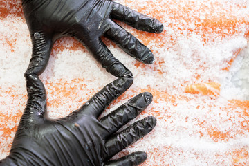 Master shusi with black hygienic gloves cleaning and preparing a huge fresh salmon.Salting the fish in a bowl. Kitchen and food concept