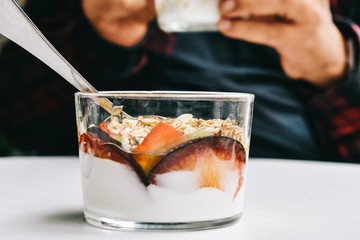 Close-up of a transparent bowl of yogurt with muesli and fresh assorted fruits and partial view of an unfocused person holding another bowl like it - Powered by Adobe