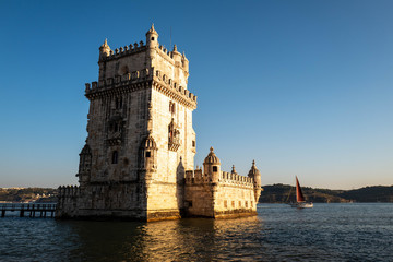 The tower of Belem in Lisbon illuminated by the setting sun with a boat passing in the background.
