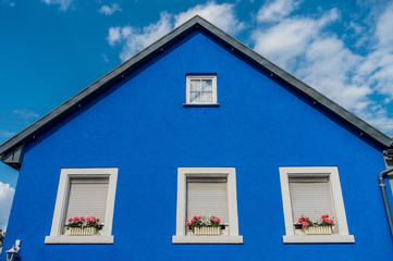 Blaues Musterhaus mit Blumenschmuck vor den Fenstern