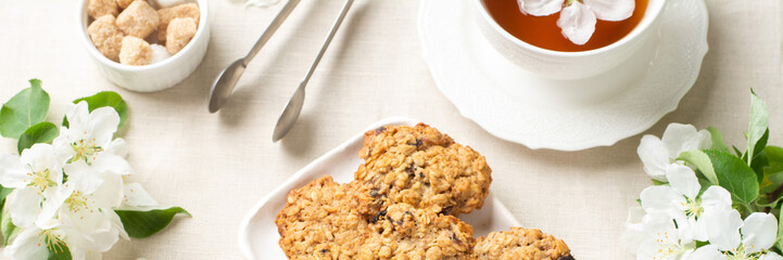 Oatmeal cookies Cookies in a white ceramic plate on a light table among flowering branches. Healthy homemade oatmeal cookies. A plate of cookies and a Cup of tea on the table. Banner