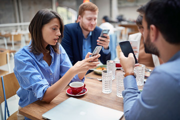 young adult businesspeople at lunch in a restaurant checking their cell phones for any good news after coronavirus. covid 19, recession, business problems concept