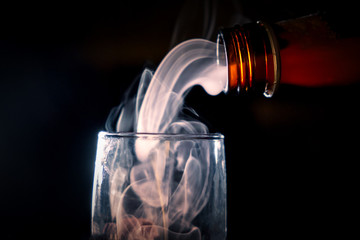 The neck of a brown bottle with alcohol overlooked a glass, from it comes to an evil spirit that...