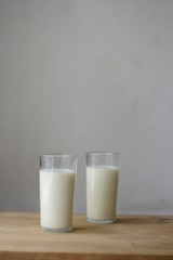 two glasses of milk stand on a wooden table against a gray wall