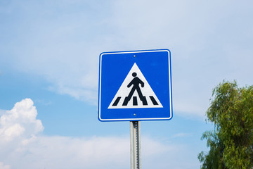 International traffic sign 'Pedestrian crossing' on clouded blue sky background. Symbolic person crosses street from right to left