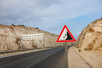 International traffic sign 'Falling rock' standing on highway road