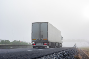 Truck with refrigerated semi-trailer driving on the highway on a thick foggy day