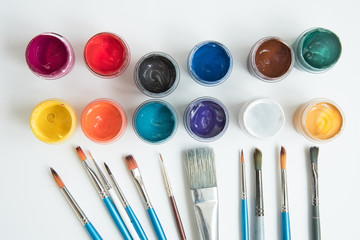 Open jars with gouache and paint brushes of different sizes. The view from the top. Background,...