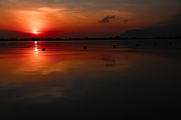 Obraz premium Cinematic red sunset sky reflected on the still waters of the Mekong River during the hot and humid summer season in Cambodia