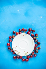 circle of cherry berries with stem on blue background and water drops top view.Beautiful food circle Frame of red ripe cherries. Arrangement of fresh berries. Flat lay.Copy space