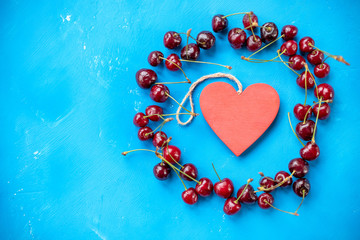 Obraz premium circle of red heart and cherry berries with stem on blue background and water drops top view.Beautiful food circle Frame of red ripe cherries. Arrangement of fresh berries. Flat lay.Copy space