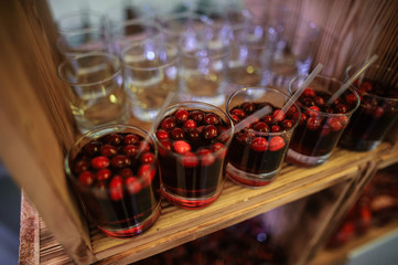 Glasses with soft drinks with red berries and without berries stand on a wooden buffet table