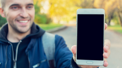 Happy man shows the screen of his phone, autumn Park, close-up, 16:9