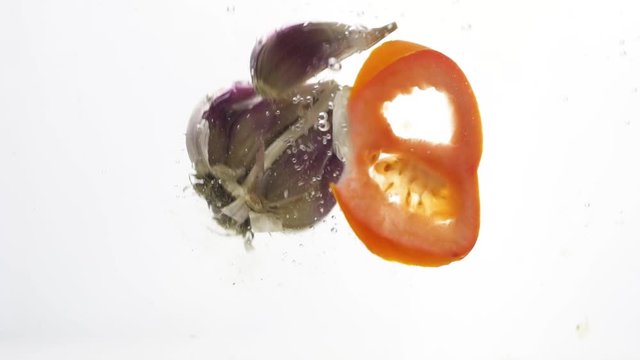 Garlic and tomato falls into water over white background
