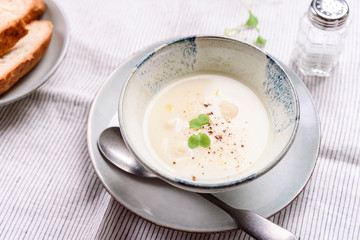 Cauliflower and Potato Cream Soup served with herbs and pepper on white linen striped tablecloth. Selective focus