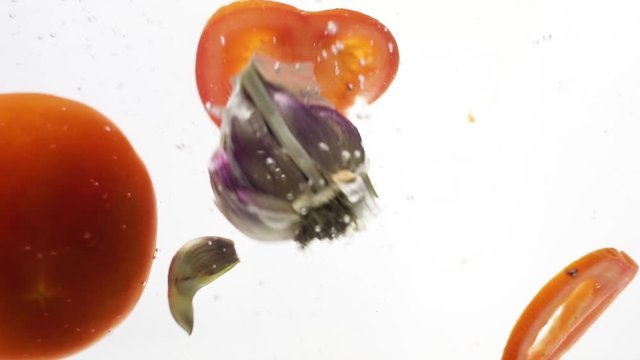 Garlic and tomato falls into water over white background