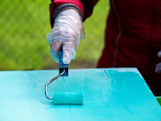 Woman's hand paints a sheet of plywood in turquoise color with a roller