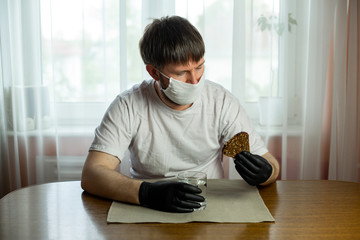 COVID-19. Young caucasian man in glasses, white mask and black gloves with a slice of bread and a...