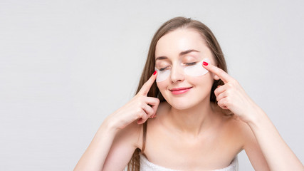 Woman shows eye patches, white background, white background, copy space, 16:9. Concept of beauty