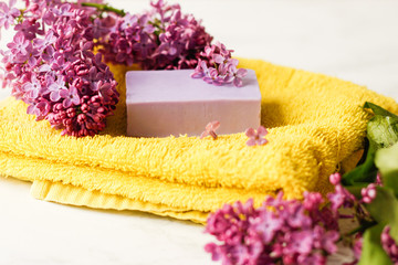 Handmade soap on a yellow terry towel and lilac flowers for spa and aromatherapy. Selective focus. Place for text.