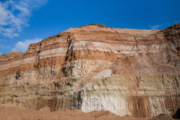 Geological cut of earth layers in industrial quarry. Its structure contains multicolored different kind of resources, such as limestone, gravel, clay, sandstone.
