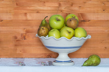 ceramic fruit bowl with apples and pears on cloth and wood tablecloth