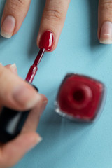 A woman painting her nails with red lacquer over blue background.