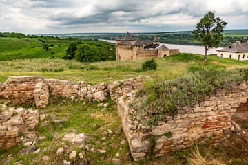Fototapeta na wymiar Khotyn Fortress castle in Ukraine, river on a background of dark clouds on a cloudy windy day in summer. Brick ruins in the foreground. Horizontal orientation.
