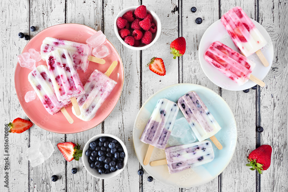 Poster table scene of homemade berry yogurt ice pops. above view with a rustic white wood background.