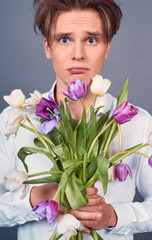 Close-up, a young man holds in a rumpled broken bouquet of tulips.