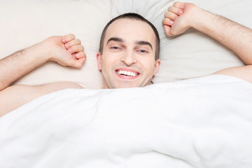 Fototapeta na wymiar Happy guy woke up in the morning in his bed. Concept of healthy sleep. Portrait, top view