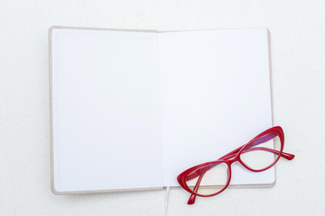Notepad and red women's glasses, white background, top view, copy space