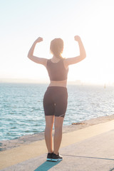 Back view of sports girl standing outdoors near the sea feeling strong