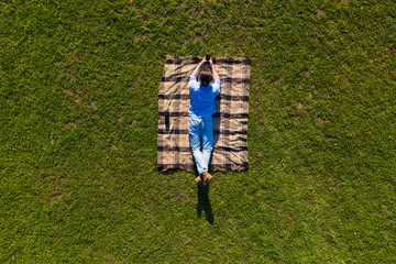Top view Young handsome man with mobile phone lying on the blanket on green grass. Aerial view.