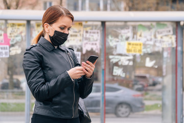 A girl in a medical mask stands alone at a stop waiting for transport. The concept of social distance and security during a pandemic