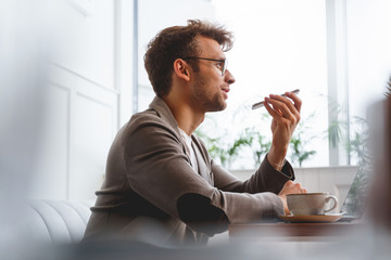Handsome gentleman using speaker while talking on cellphone in cafe