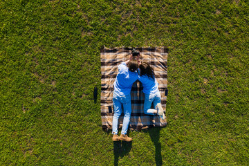 Top view of young couple lying on the blanket on green grass holding photo camera and watching...