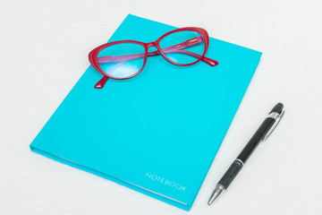 Blue notebook, pen and red women's glasses, white background, top view, copy space