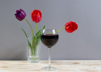Red wine glass and tulips in  vase  on  wooden background