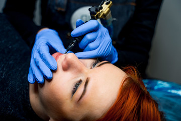 Young woman having permanent makeup on lips in beauty salon. Close up