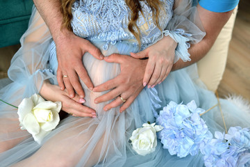 Waiting for the baby. Pregnant woman in a blue dress with a heart from father hands on her stomach, 40 weeks.