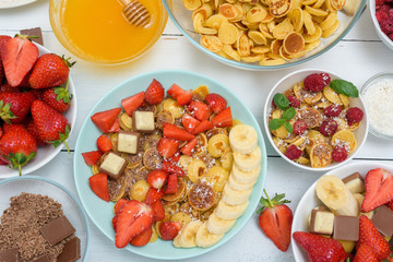mini pancake cereal bowl with fresh strawberries banana chocolate, coconut shavings and honey in small plates. the view from the top . the trend of self-isolation