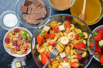 mini pancake cereal bowl with fresh strawberries banana chocolate, coconut shavings and honey in small plates. the view from the top . the trend of self-isolation