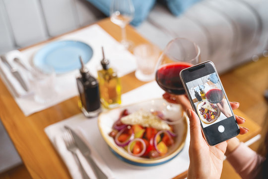 Young lady taking picture of food and wine with smartphone