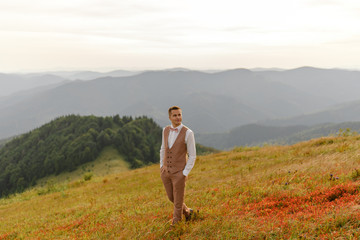 Naklejka na ściany i meble The groom is walking alone on the background of autumn mountains.