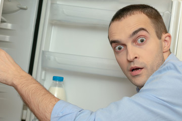 Shocked young man looking for food in the refrigerator, side view