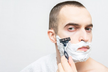 Handsome man shaves on camera with shaving foam, white background