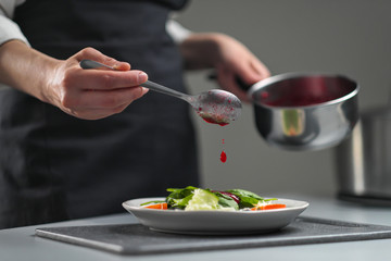 A female chef in a white uniform and a black apron in the restaurant kitchen. The cook pours red cranberry salad sauce. Making and decorating food.